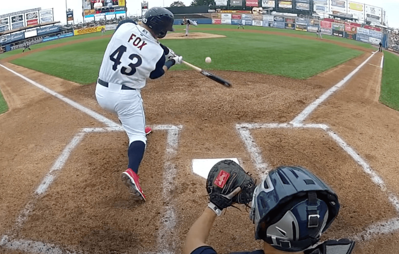 A baseball hitter making contact with a baseball from the view of an umpire. The ball appears to be going directly back at the pitcher.